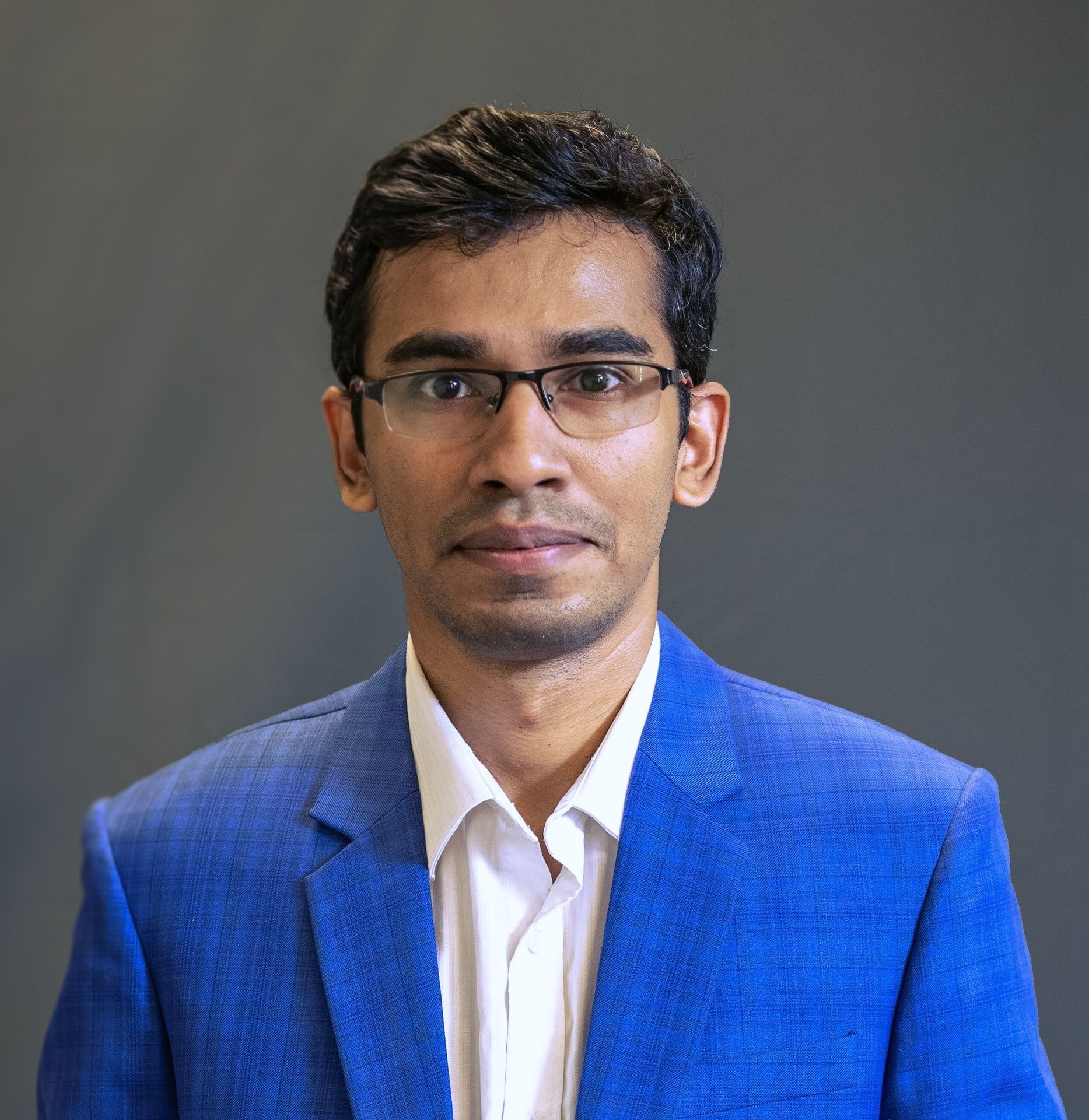 Person wearing glasses and a blue suit jacket against a plain background.